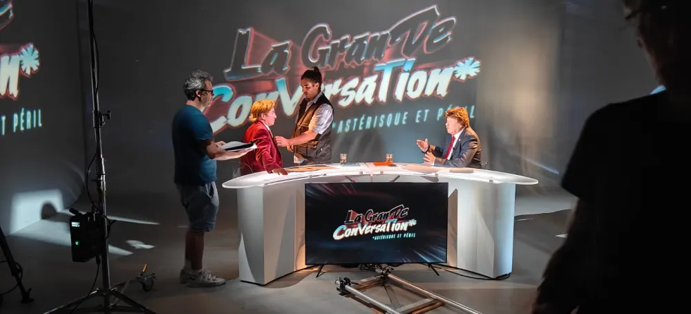 Le plateau de « La Grande Conversation », le logo de l'émission projeté au mur : on installe le micro d'Arthur Green, en veste rouge, à la table blanche
